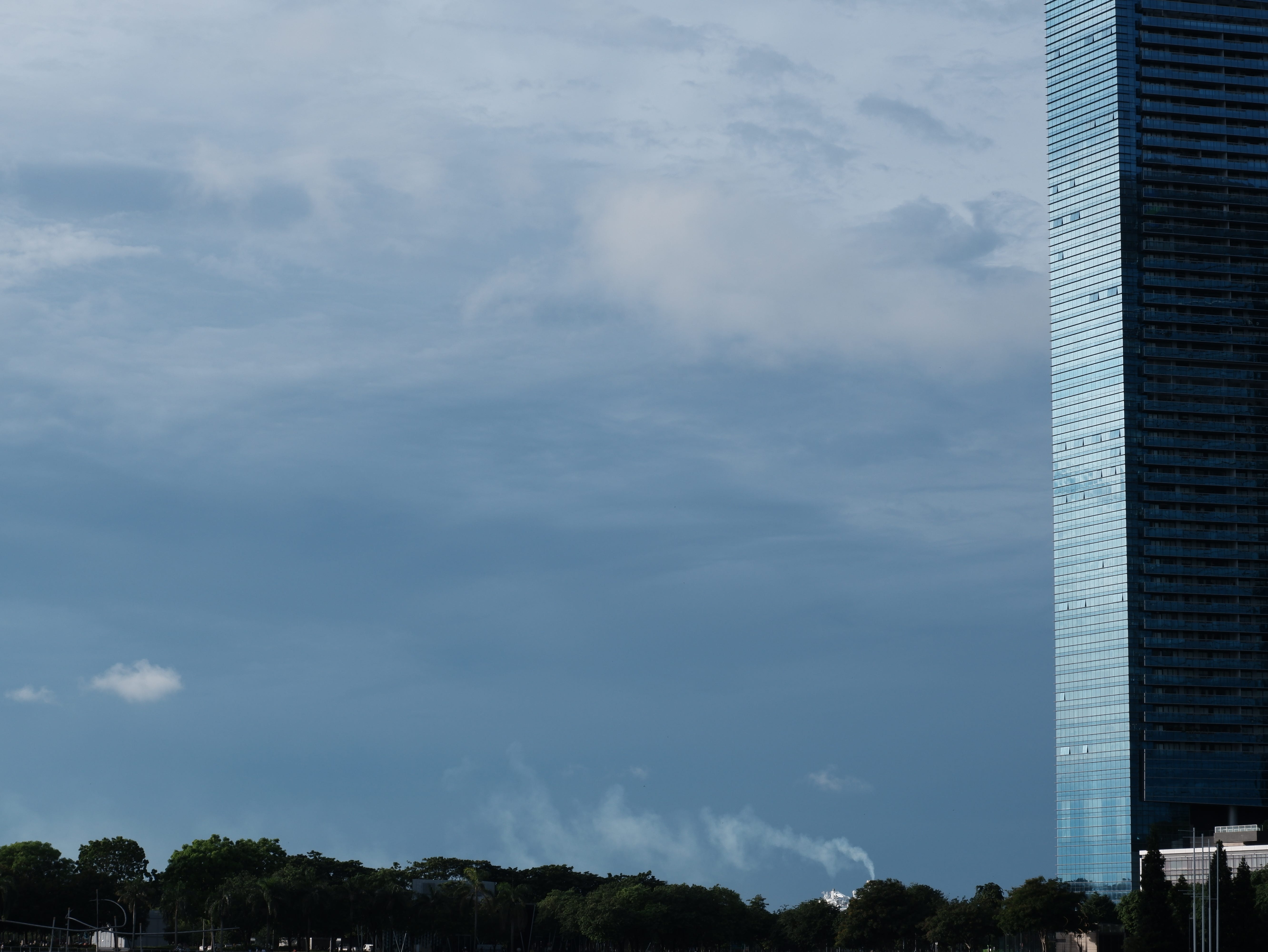 A plume of white smoke rises from a distant building across the Marina Bay. The smoke almost resembles the clouds, but its rapid motion gives it away.