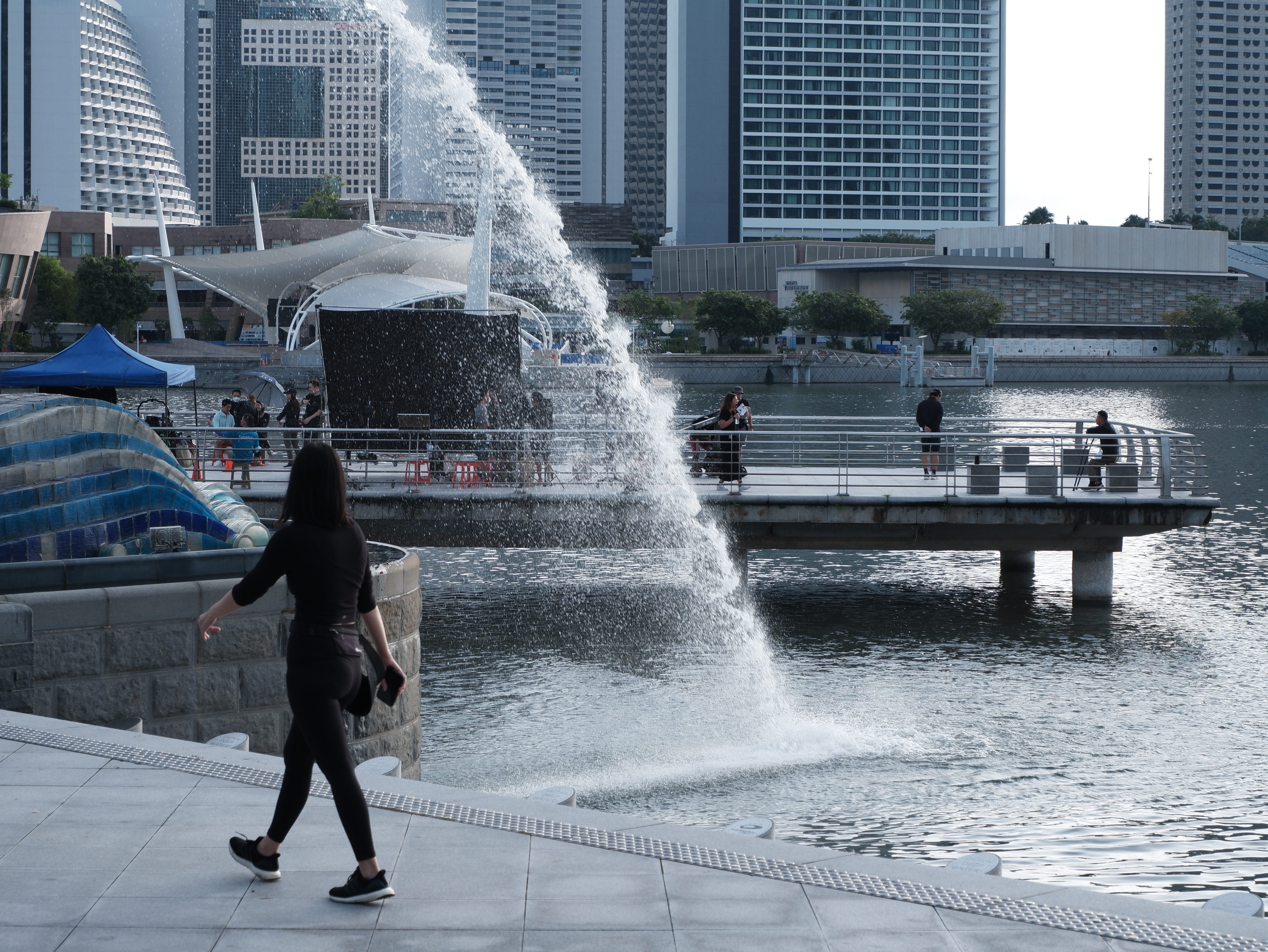 A jogger looks on curiously at at the filming as she walks by. Behind her, the film crew members appear to taking a break.