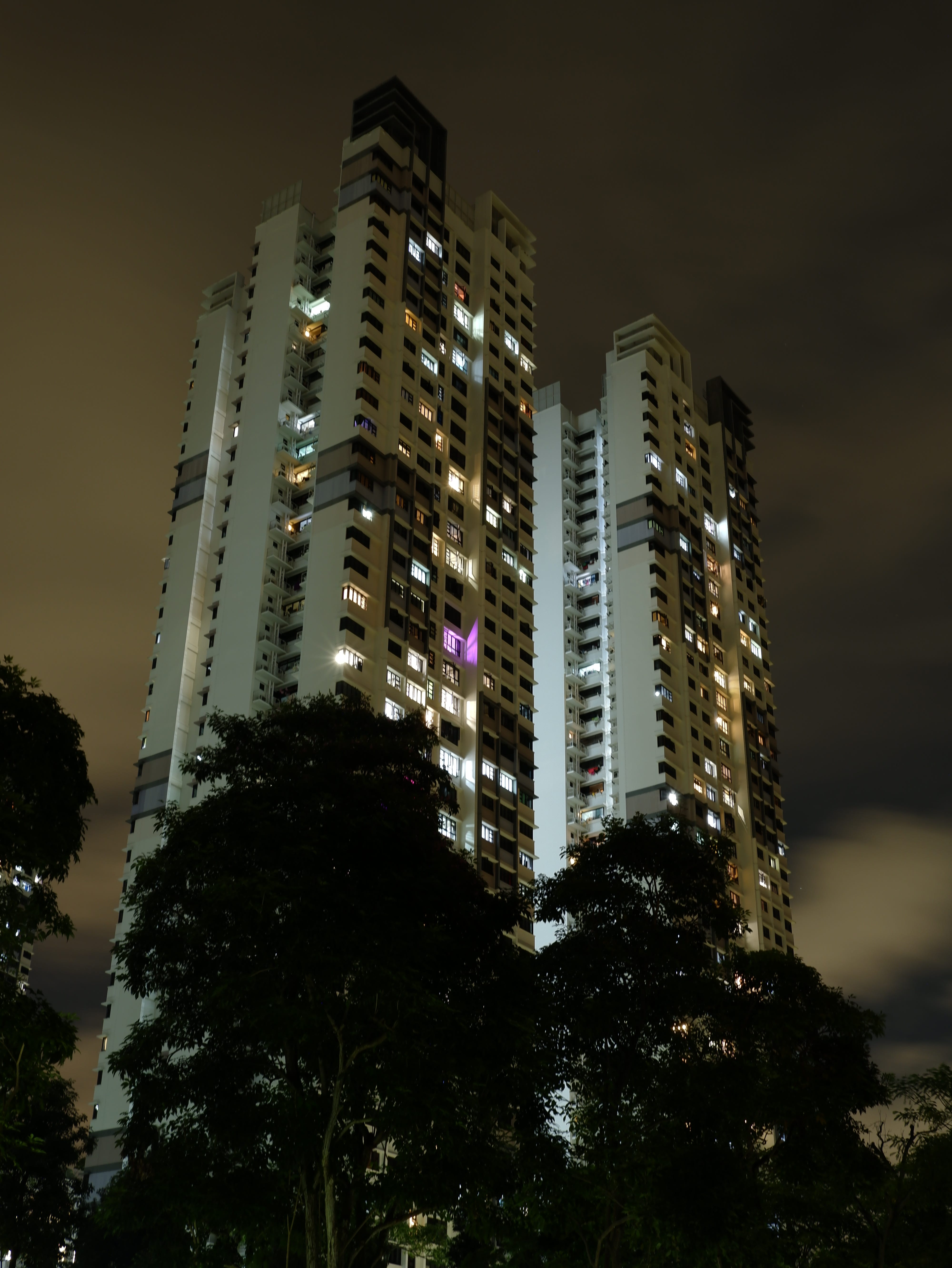 Windows of an apartment building lit up at night. The magenta glow of grow lights is seen on one of the windows.
